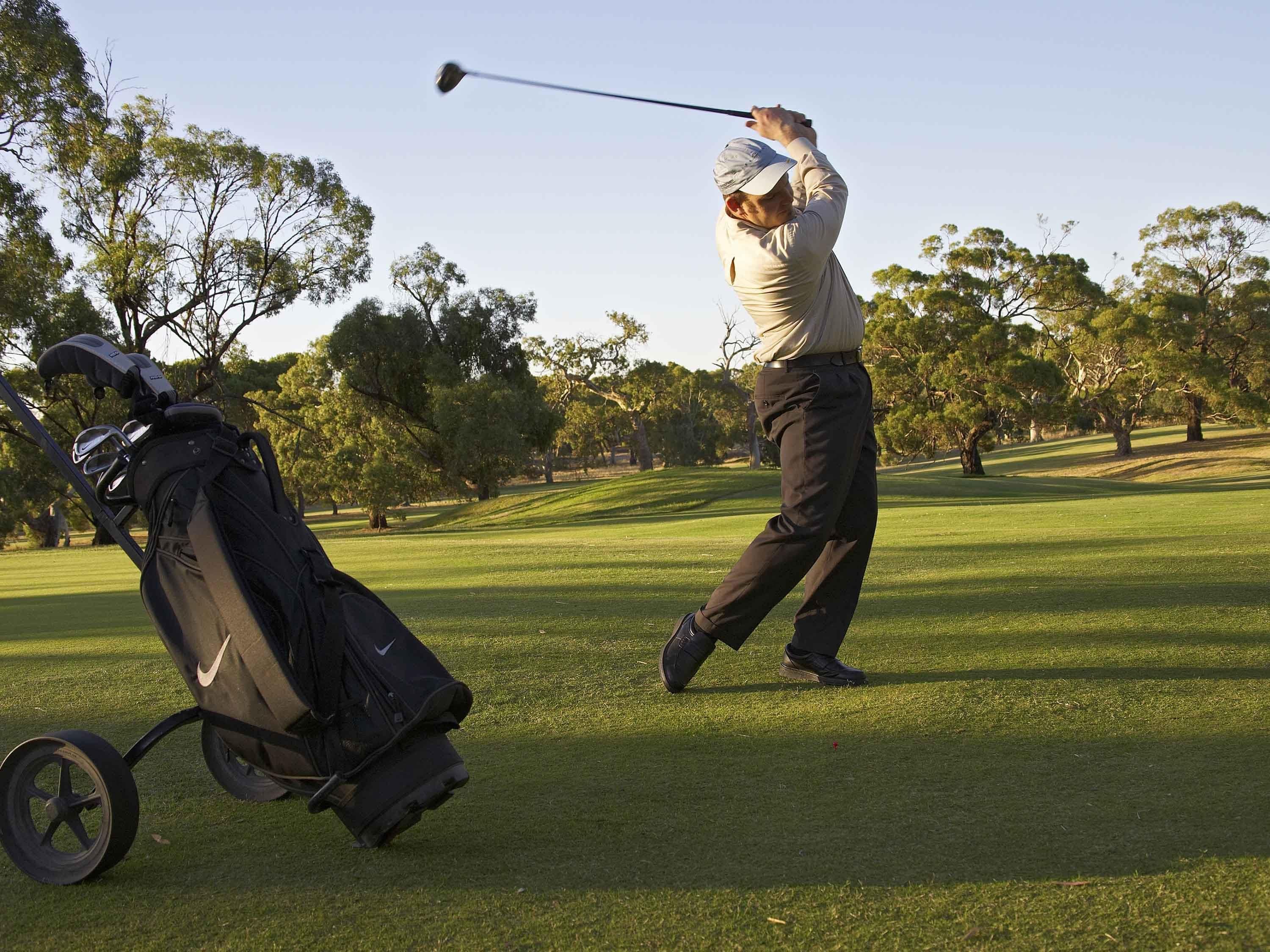 Eine Person spielt Golf, ein Bag mit Schlägern steht auf dem Boden.