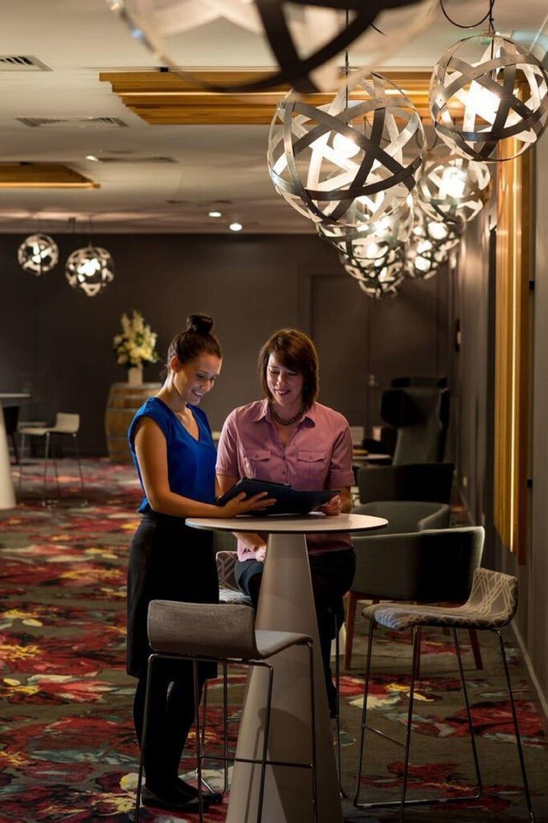 A modern hotel room with a round table, two chairs, and a decorative hanging light fixture.