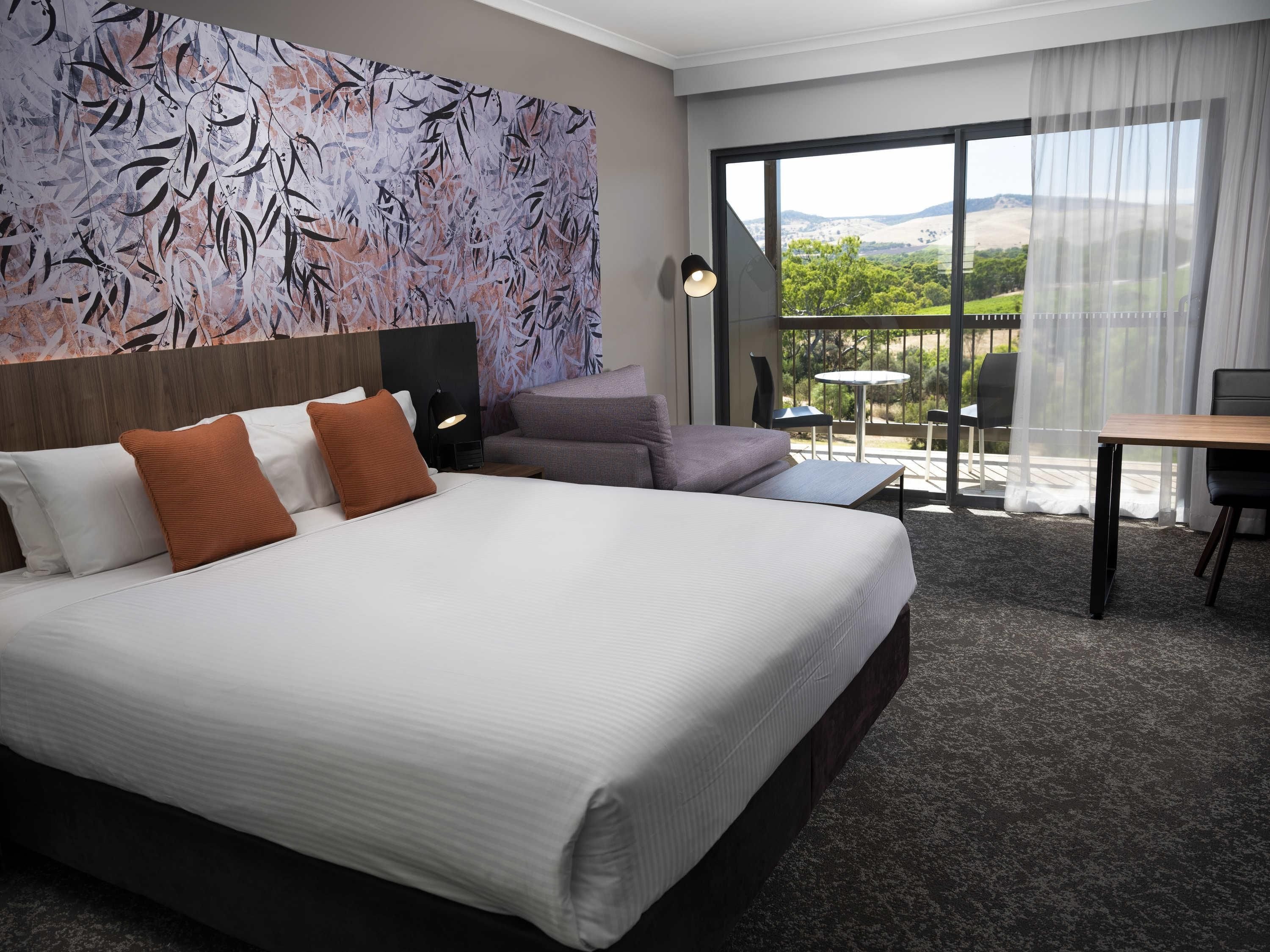 A hotel room with a large bed, a sofa, a desk, and a balcony with a view.