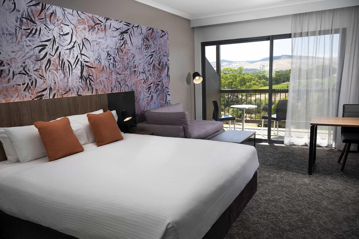 A hotel room with a large bed, a sofa, a desk, and a balcony with a view.