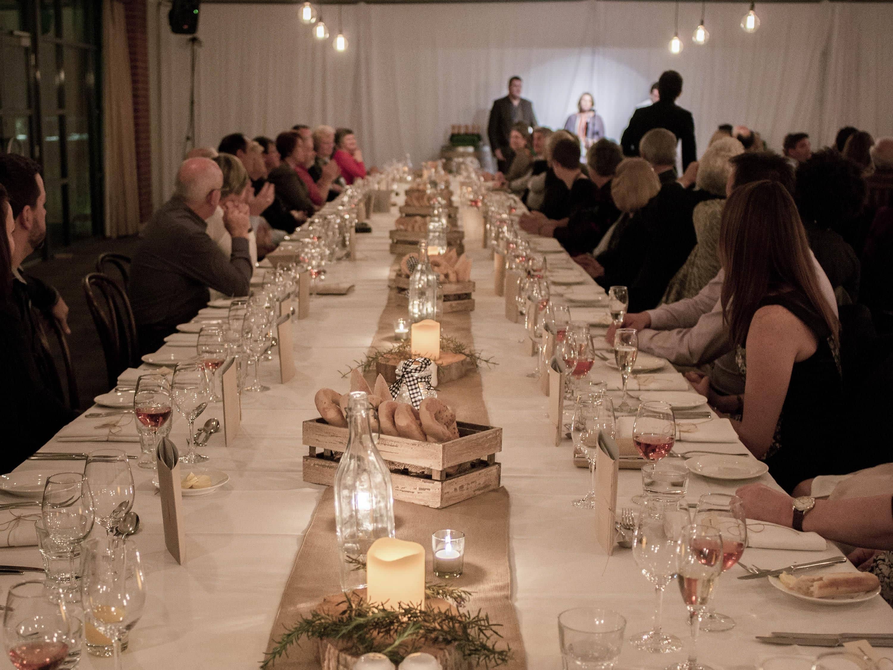 Una larga mesa de banquete dispuesta para un evento formal, con múltiples invitados sentados a ambos lados.