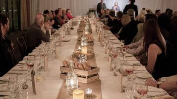 Una larga mesa de banquete dispuesta para un evento formal, con múltiples invitados sentados a ambos lados.