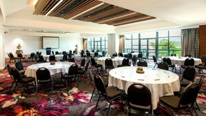 A conference room with multiple round tables, black chairs, and a large screen at the front.