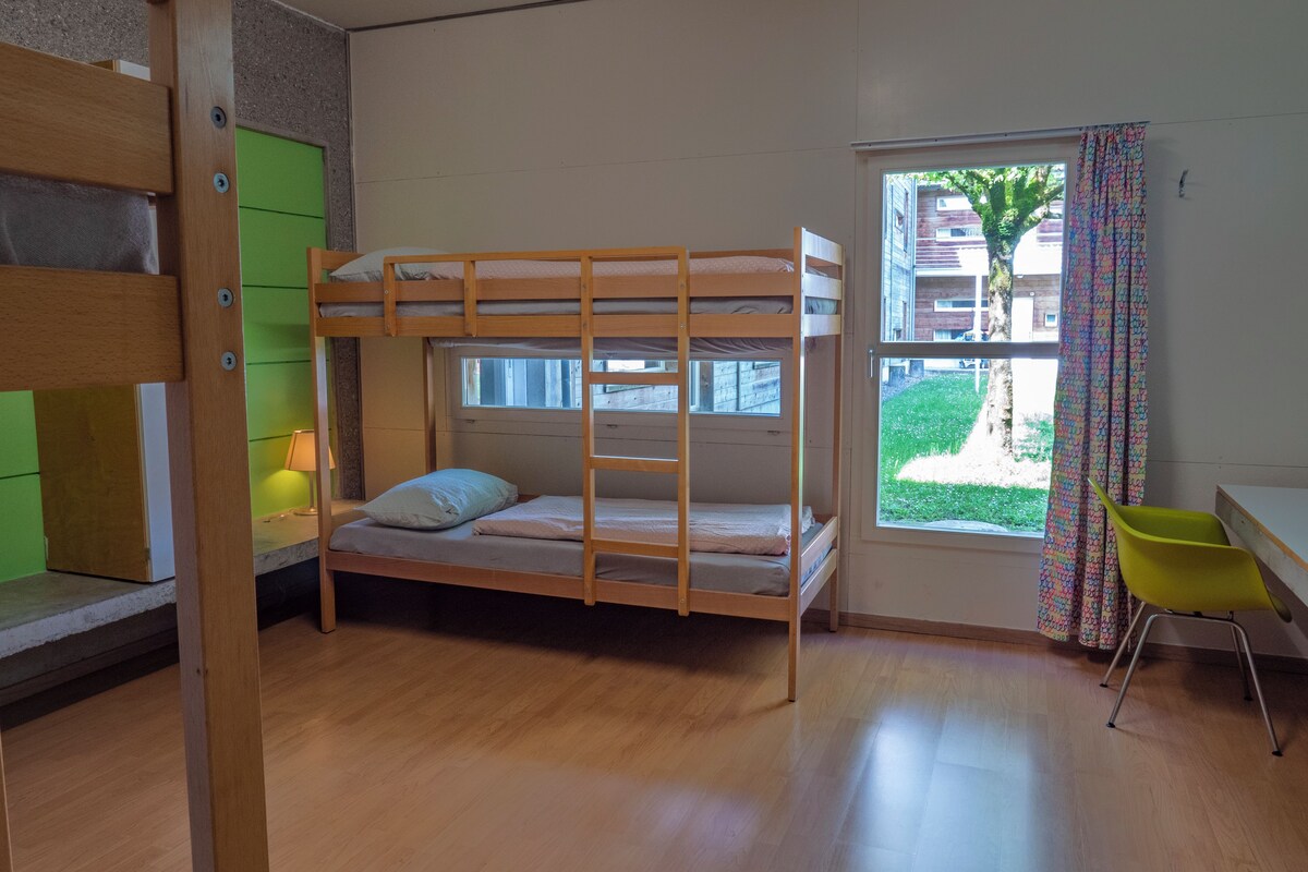 A bunk bed room with a window, a desk, and a chair.