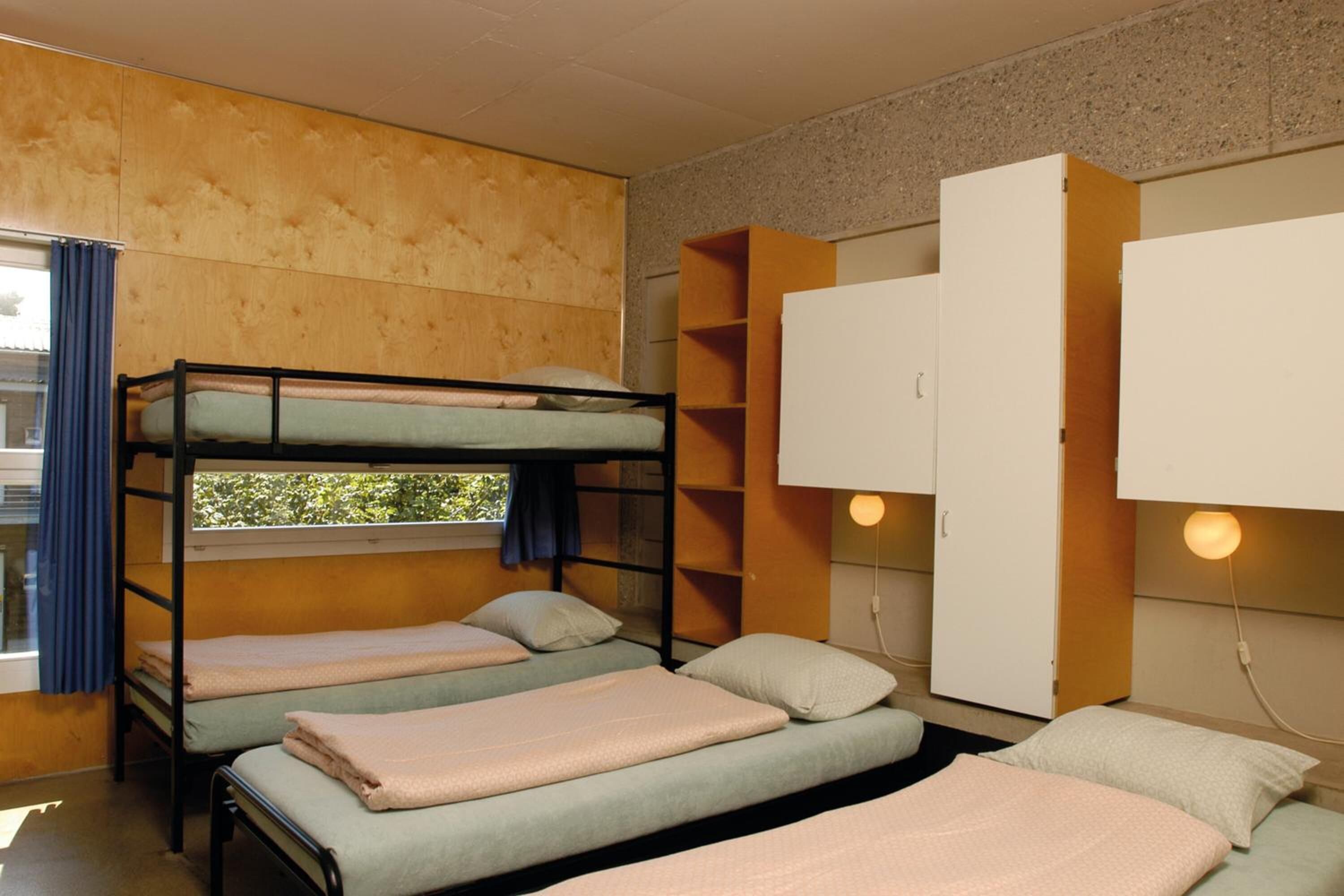 Ein Schlafsaalzimmer mit Etagenbetten, einem Kleiderschrank und einem Fenster mit Vorhängen.