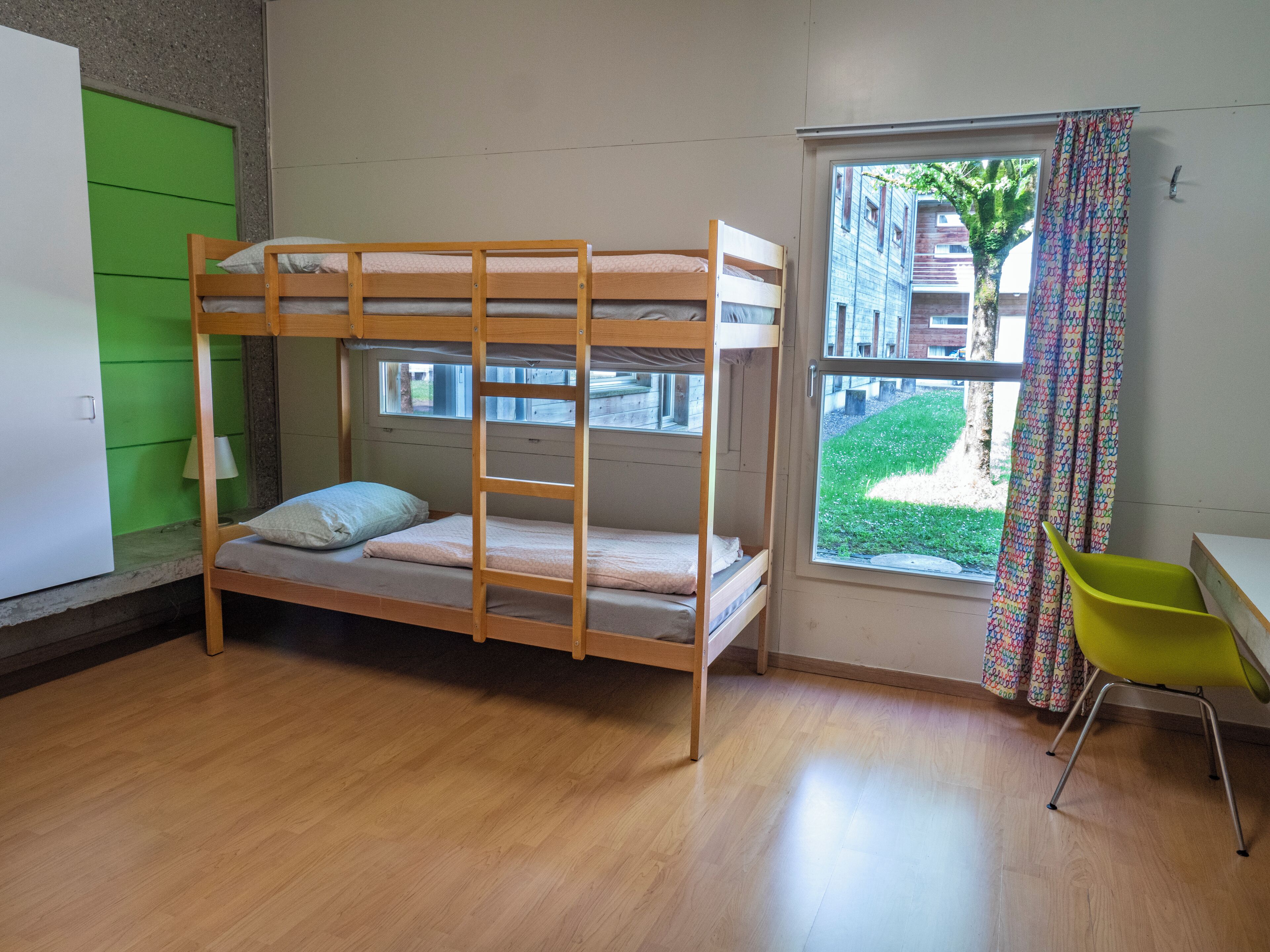 A bunk bed room with a window, a green wall, and a yellow chair.