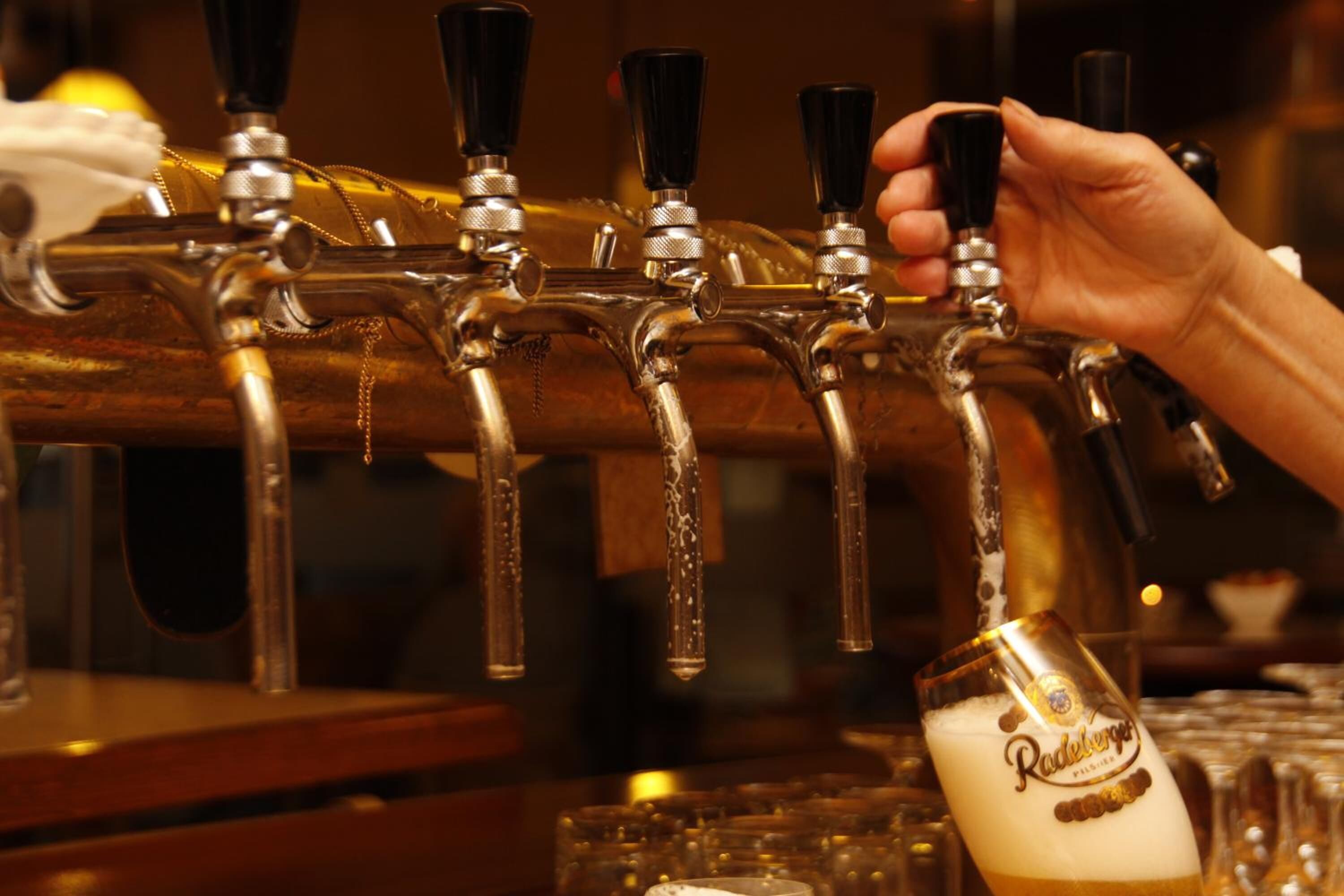 A hand operating a beer tap with a glass of beer in front of it.