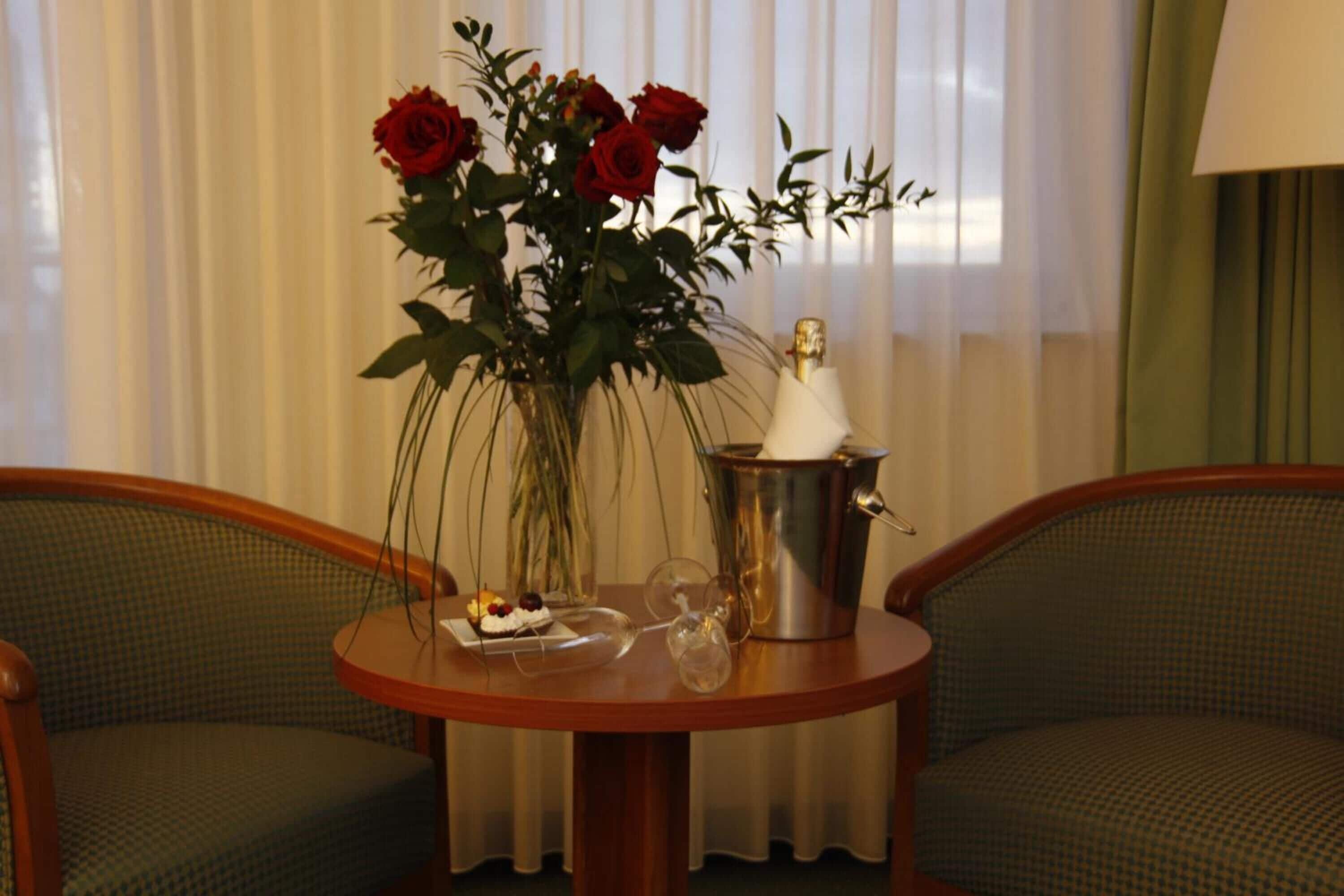 A table with a vase of red roses, a champagne bottle, and a glass of champagne.