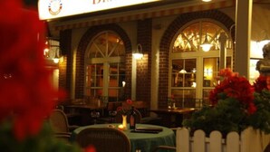 An outdoor seating area with tables and chairs, a white picket fence, and a brick building with arched windows. - Hotel Kaiserhof (Wesel)
