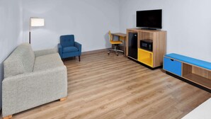 A modern living room with a sofa, a blue armchair, a wooden cabinet with a TV, and a desk with a chair. - Days Inn & Suites by Wyndham Siler City (Siler City)