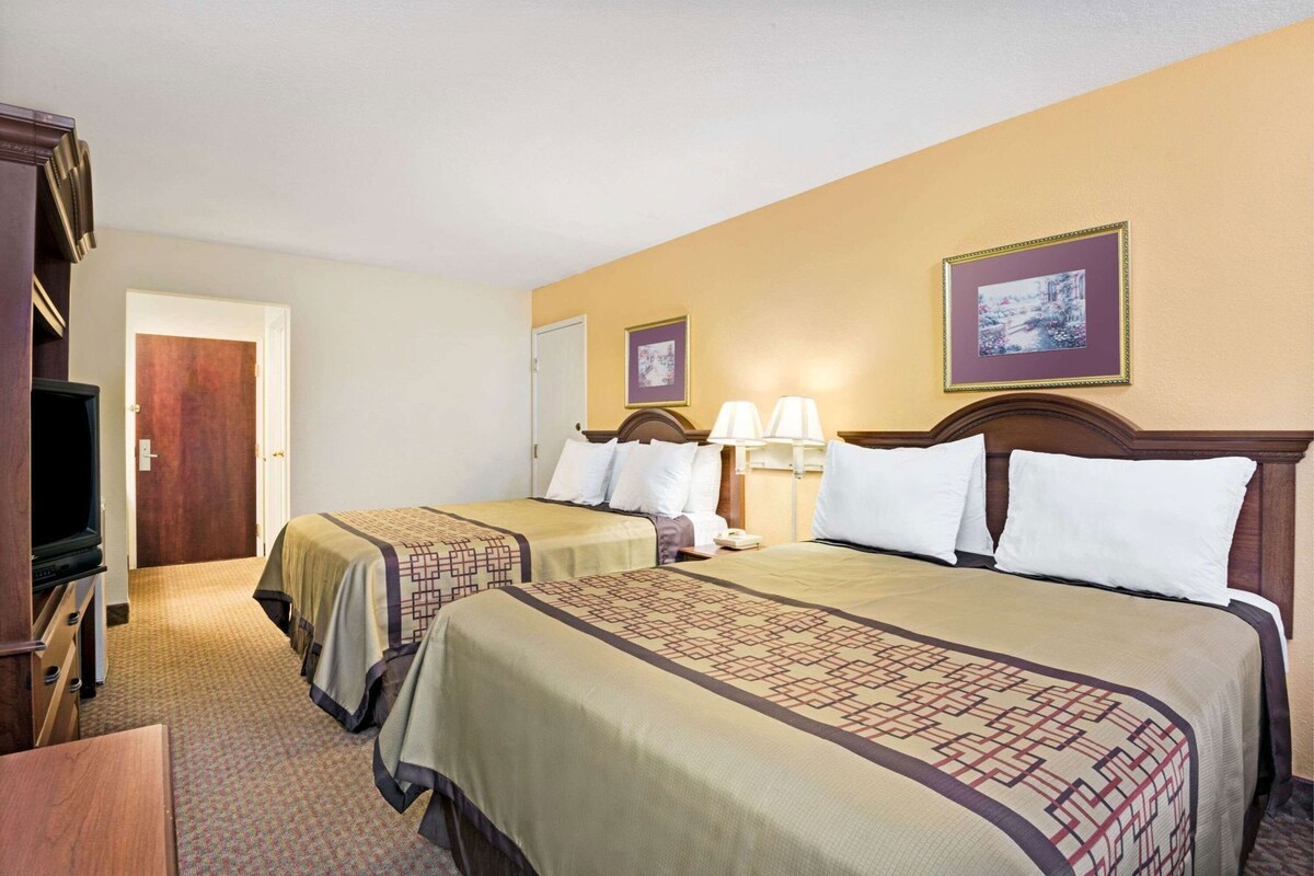 A hotel room with two beds, a television, a door, and a framed picture on the wall.