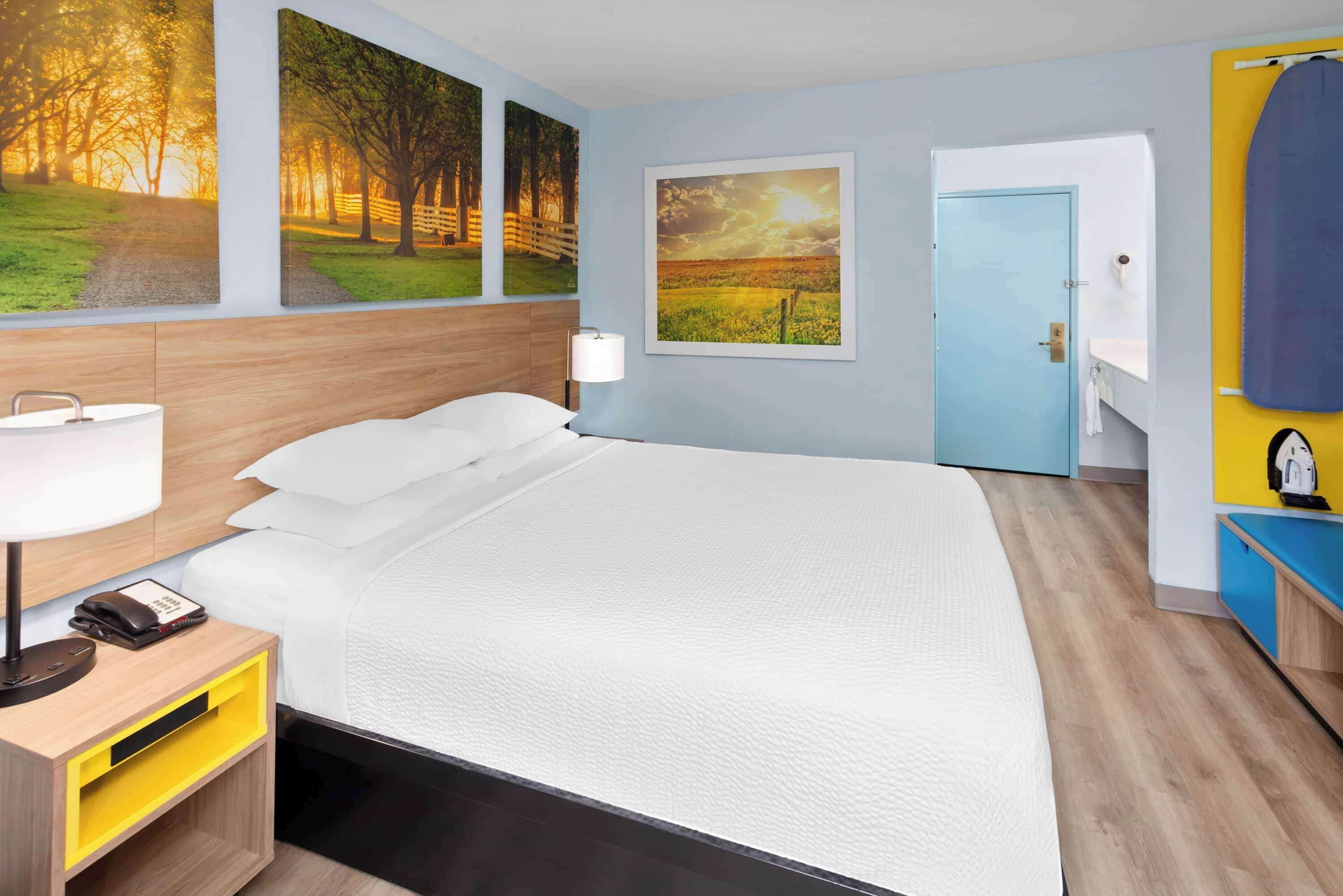 Una camera d'albergo con un letto, un comodino con una lampada, un telefono e una parete con tre quadri di paesaggi.
