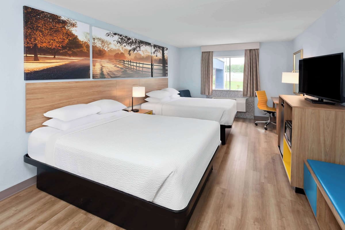 Habitación de hotel con dos camas, televisión, escritorio con silla y ventana grande.