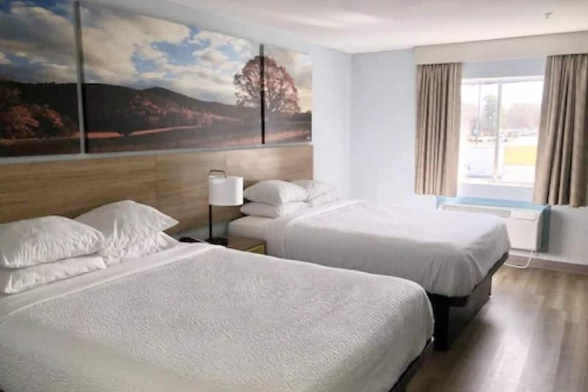 Una habitación de hotel con dos camas, un ventanal con cortinas y un cuadro en la pared.
