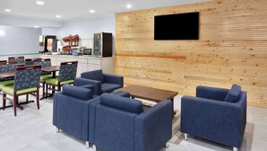 A modern dining area with blue upholstered sofas and chairs, a wooden wall with a mounted TV, and a coffee machine. - Days Inn & Suites by Wyndham Siler City (Siler City)