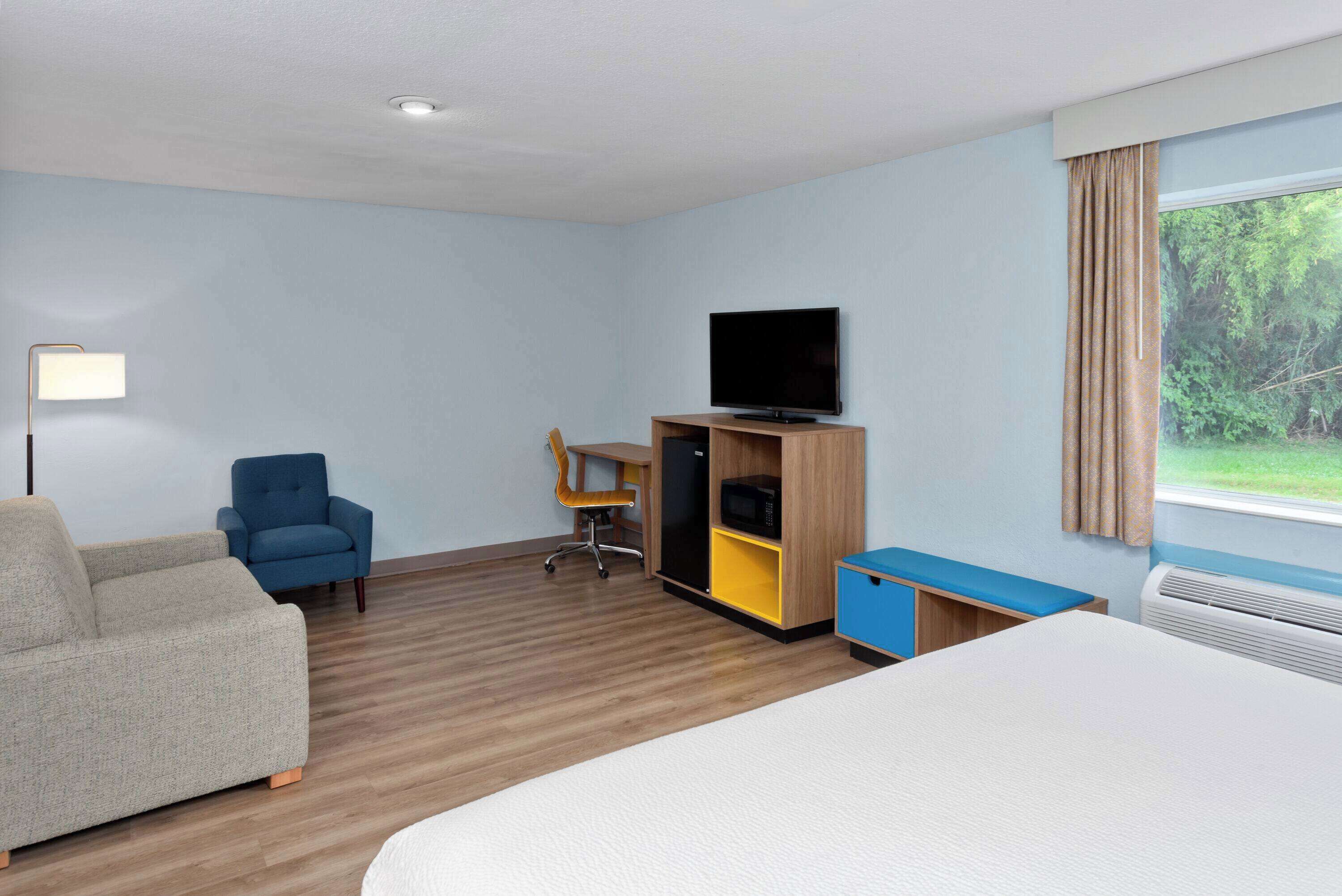 A hotel room with a bed, a sofa, a desk with a chair, a television, and a window with curtains.