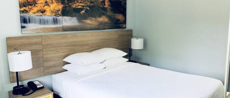 Quarto de hotel com cama, mesa de cabeceira com abajur, telefone e quadro de uma cascata.