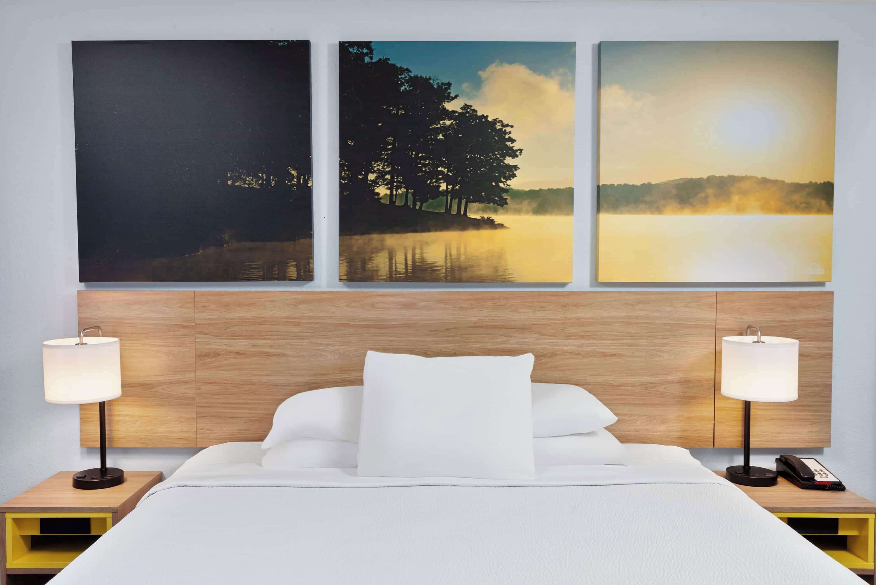 A hotel room with a bed, two bedside tables with lamps, and three framed pictures on the wall.