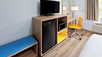 Hotelkamer met televisie, bureau met stoel, bankje, magnetron en koelkast.
