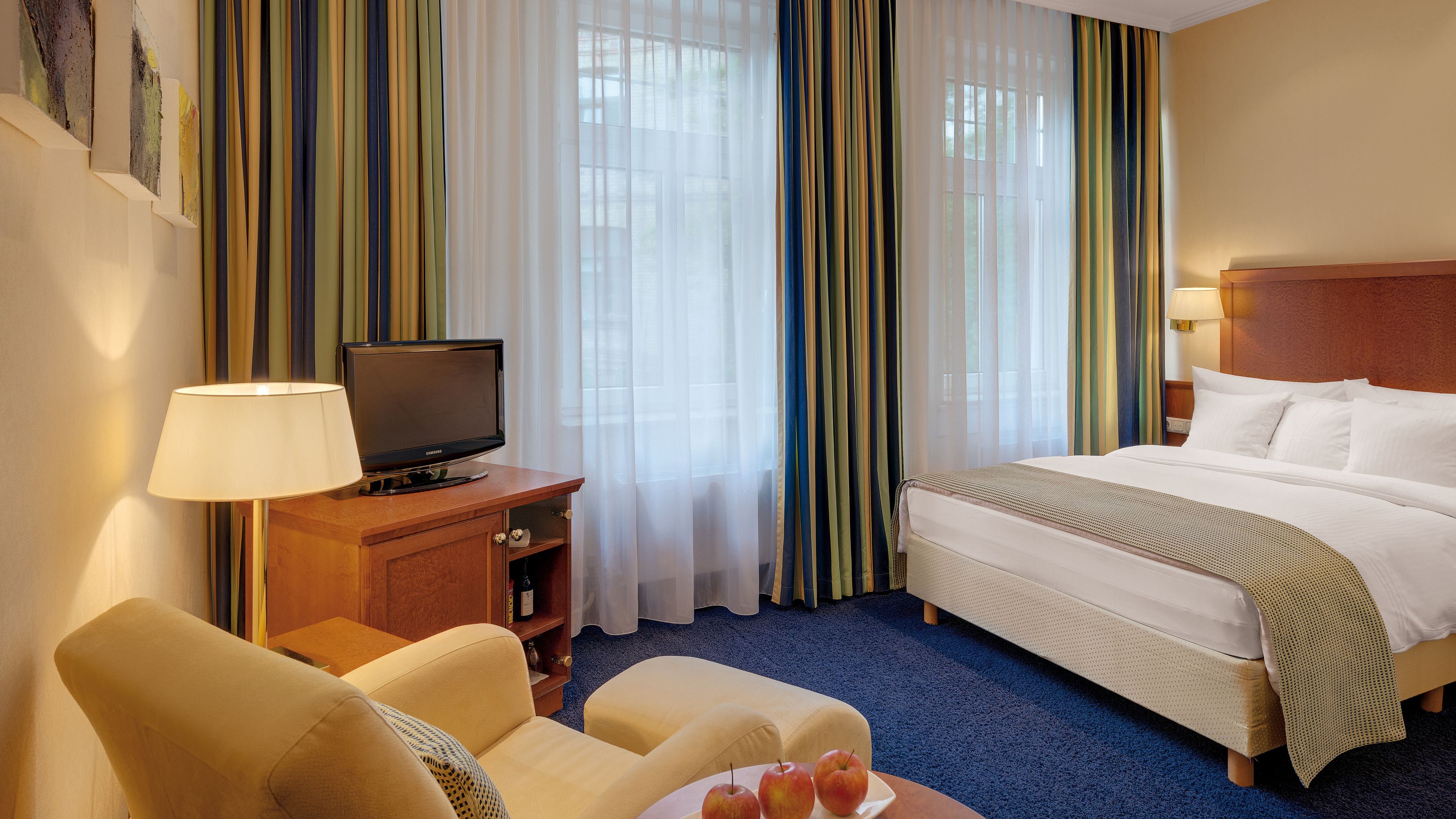 Een hotelkamer met een bed, een televisie op een houten kast, een bureau met een lamp en een stoel.