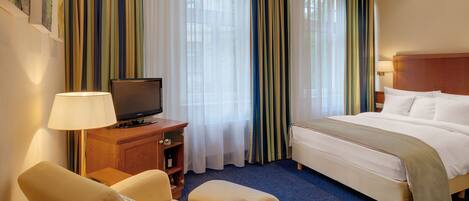 A hotel room with a bed, a television on a wooden cabinet, a desk with a lamp, and a chair.