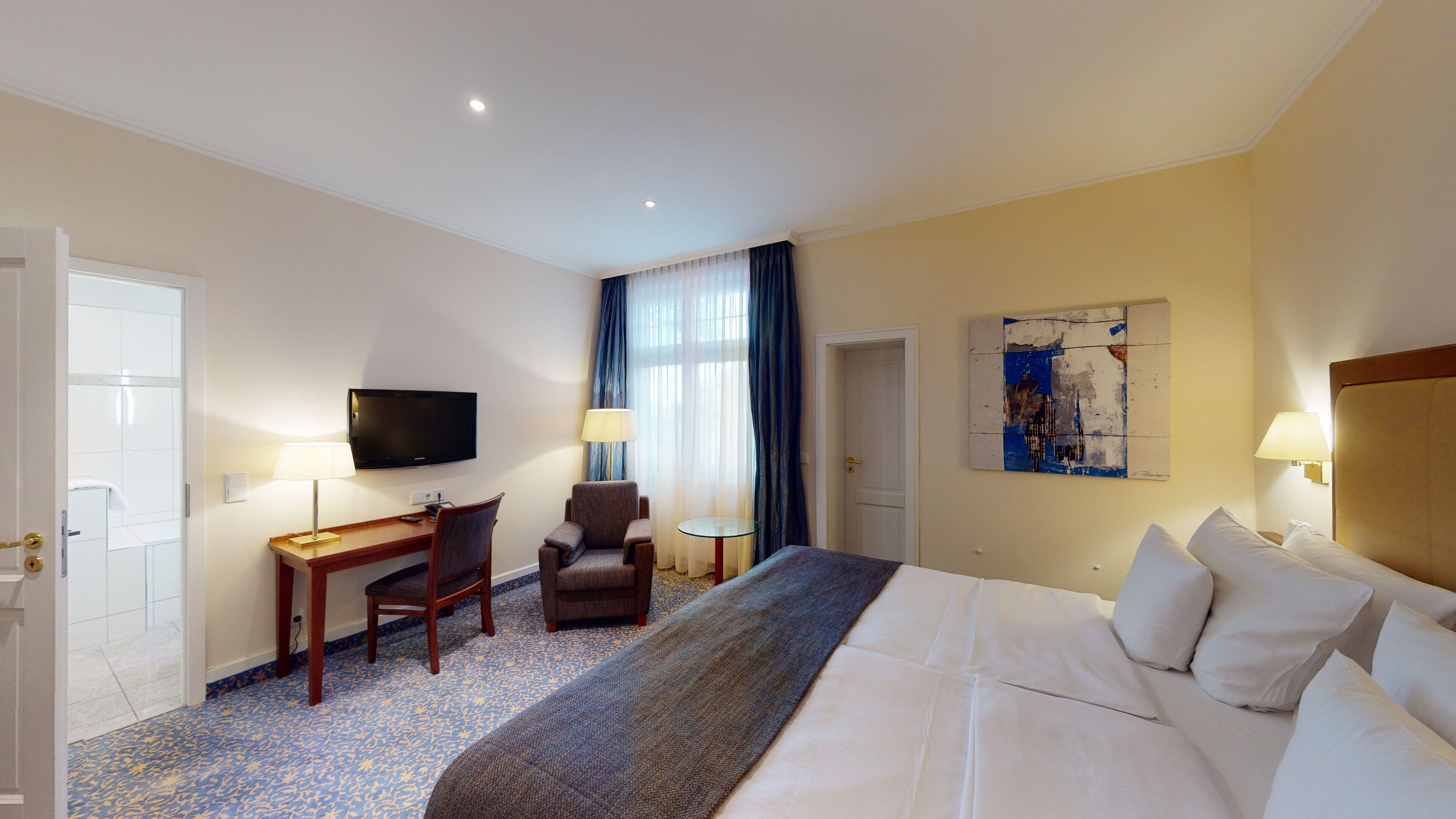 A hotel room with a bed, a desk, a chair, a television, and a painting on the wall.