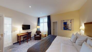 A hotel room with a bed, a desk, a chair, a television, and a painting on the wall.