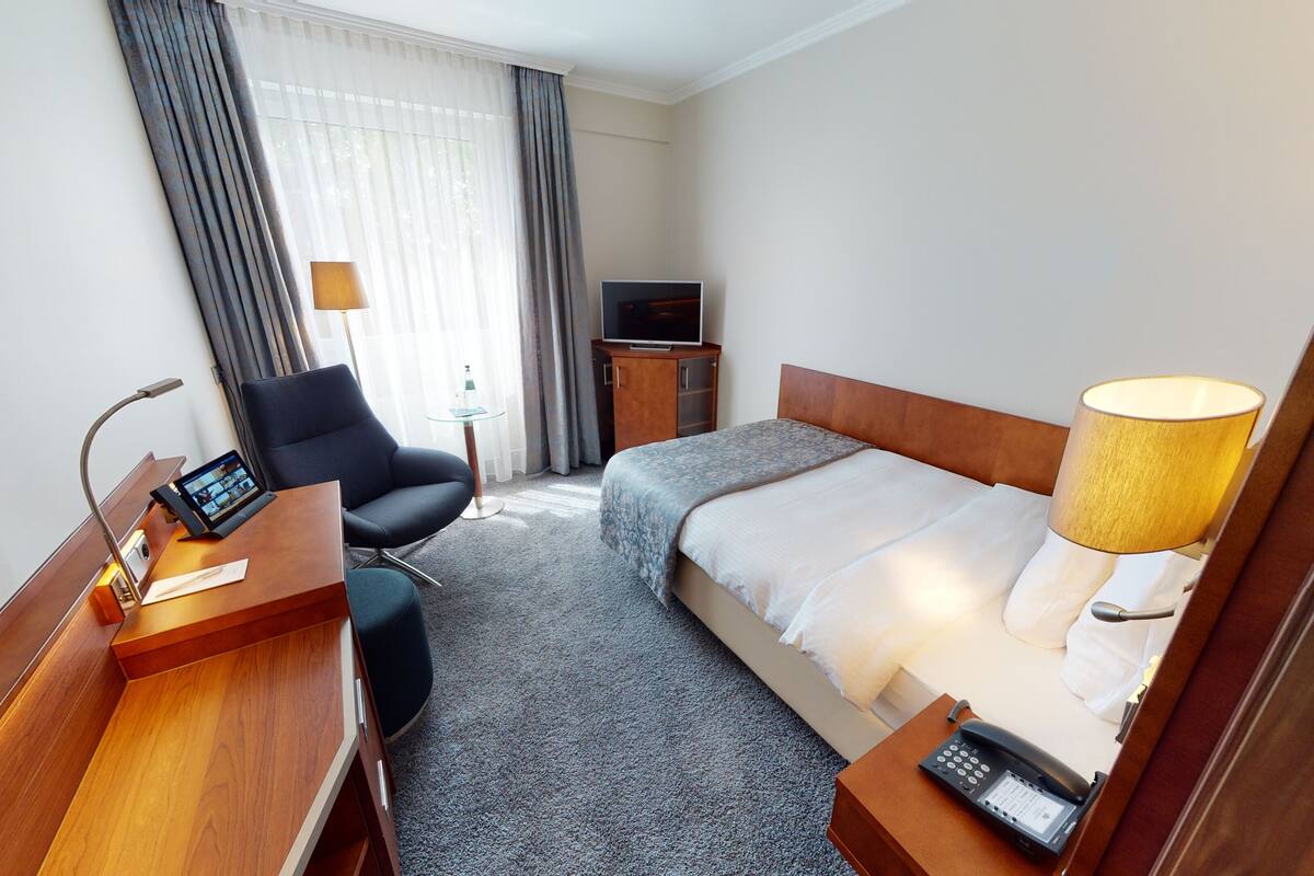 Une chambre d’hôtel comprenant un lit, un bureau avec un ordinateur, une chaise, une télévision et une lampe.