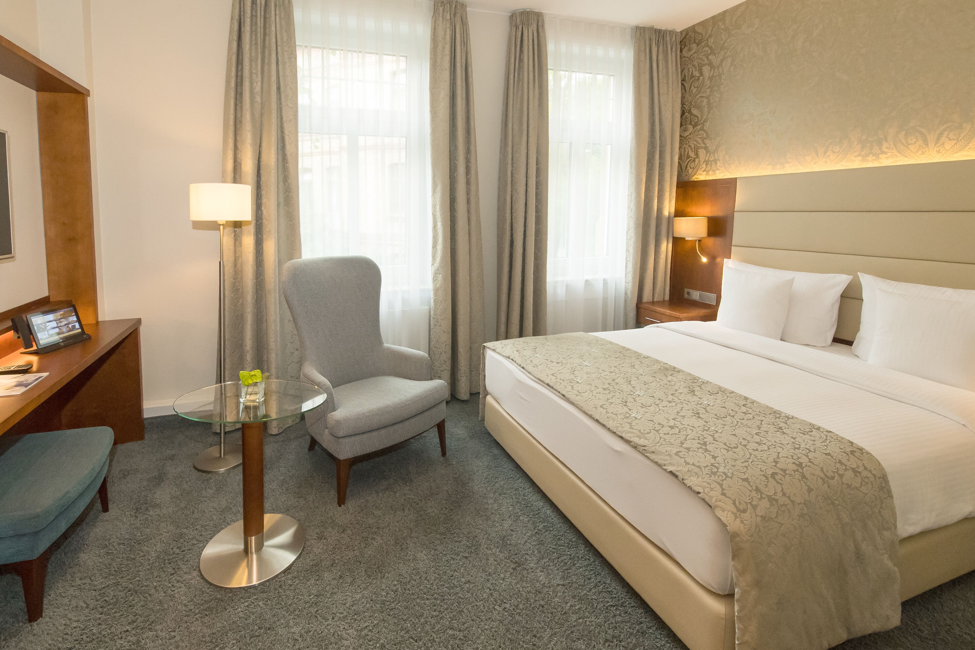 Una habitación de hotel con cama, escritorio, silla, mesita y lámpara.