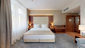 Quarto de hotel com uma cama grande, uma escrivaninha, duas mesas de cabeceira com abajures e um guarda-roupa.