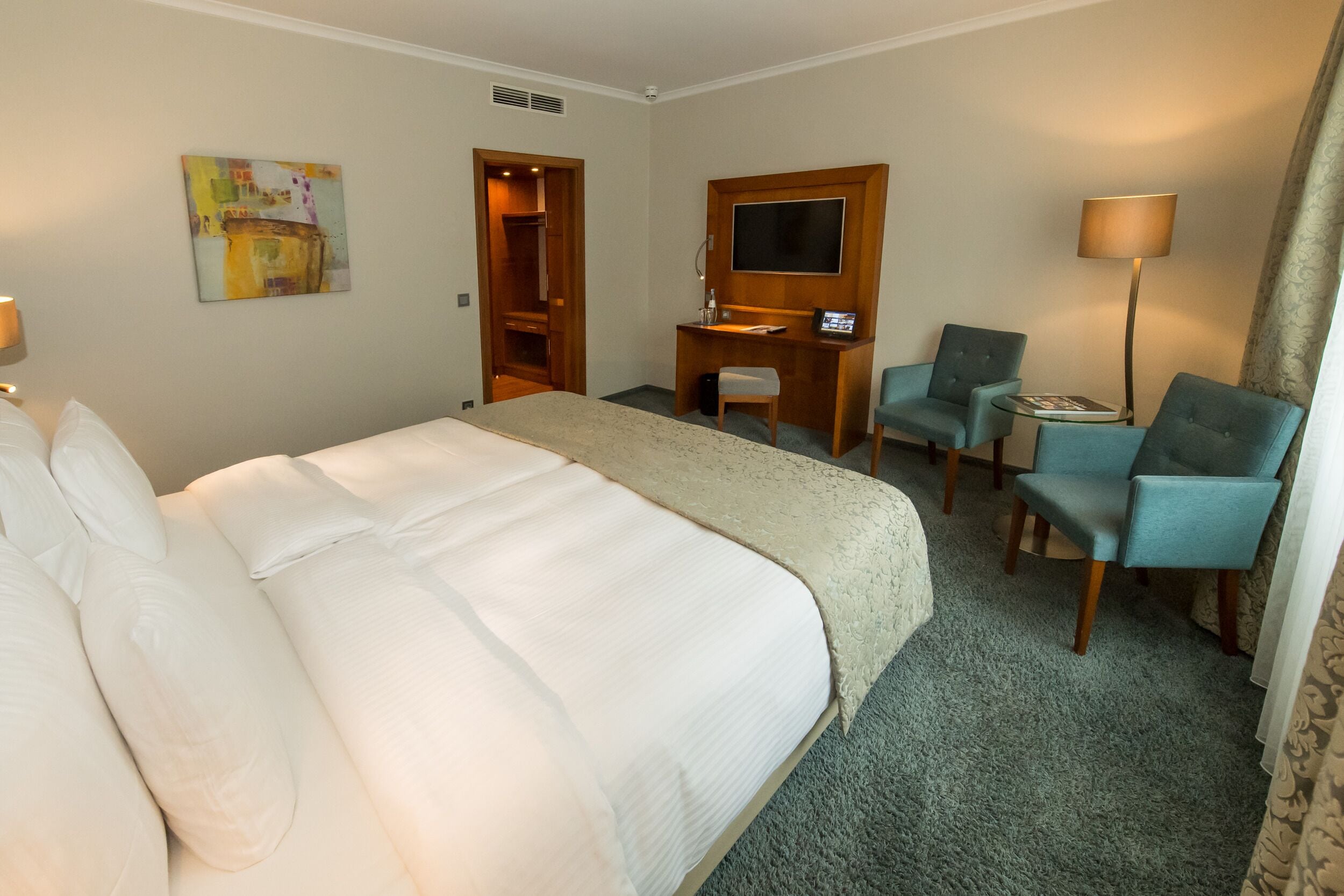 Quarto de hotel com uma cama grande, uma escrivaninha com cadeira, televisão e abajur.