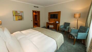 Quarto de hotel com uma cama grande, uma escrivaninha com cadeira, televisão e abajur.