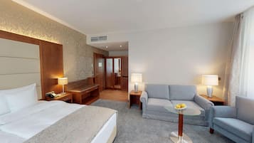 Ein Hotelzimmer mit einem Bett, zwei Sesseln, einem Sofa, einem Glastisch und einem Schreibtisch mit einer Lampe.