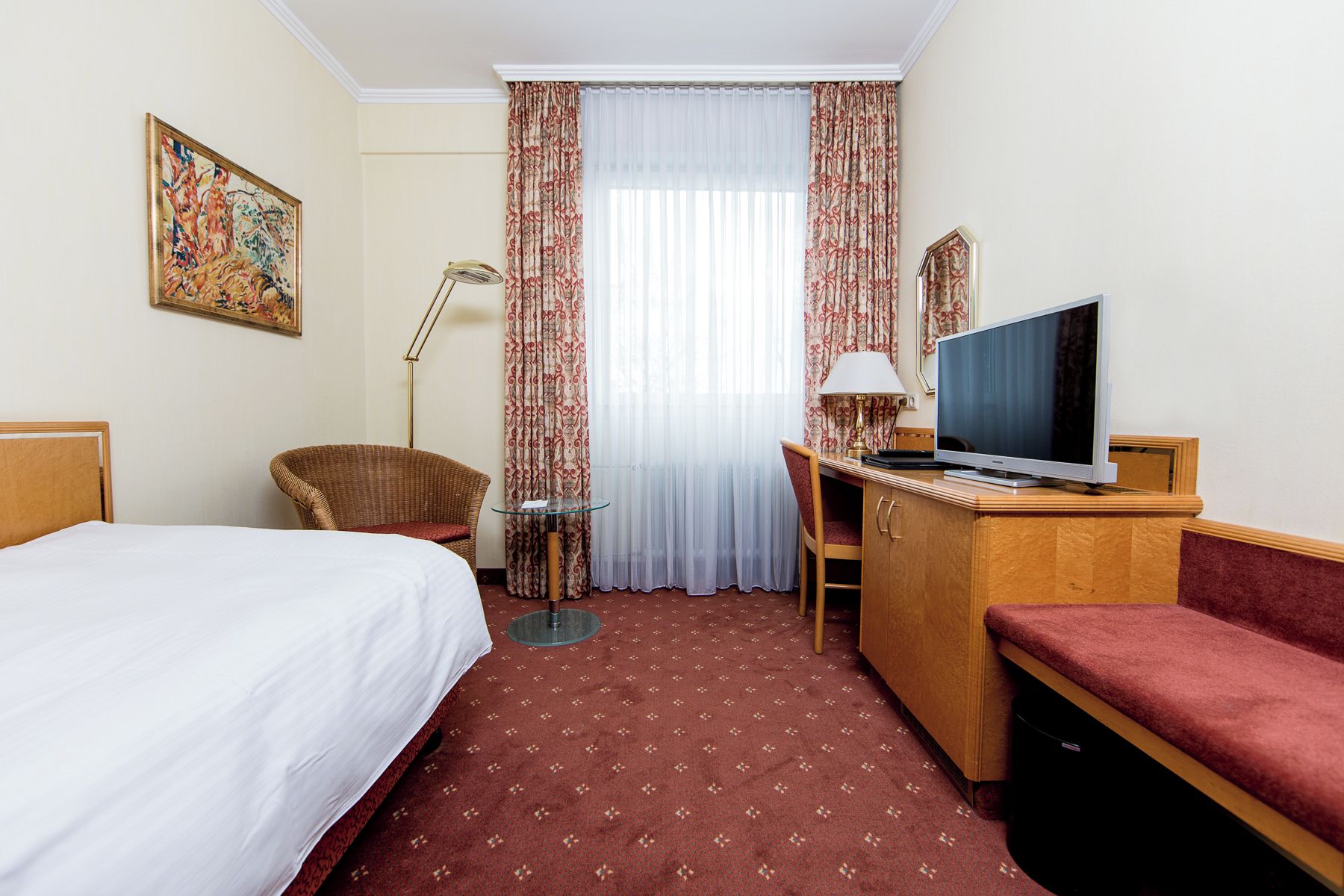 Una camera d'albergo con un letto, una scrivania, un televisore, una sedia e una lampada da terra.