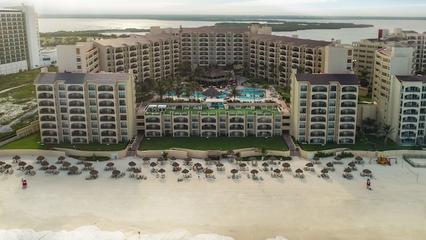 Un resort con varias edificaciones, un área de piscina central y una playa con tumbonas.