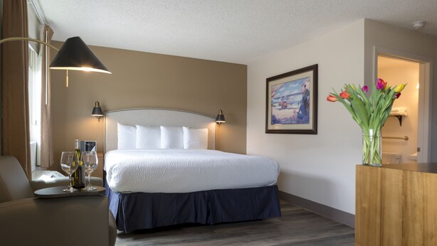 A hotel room with a bed, bedside lamps, a framed picture on the wall, and a vase with flowers. - Hotel Focus SFO (South San Francisco)
