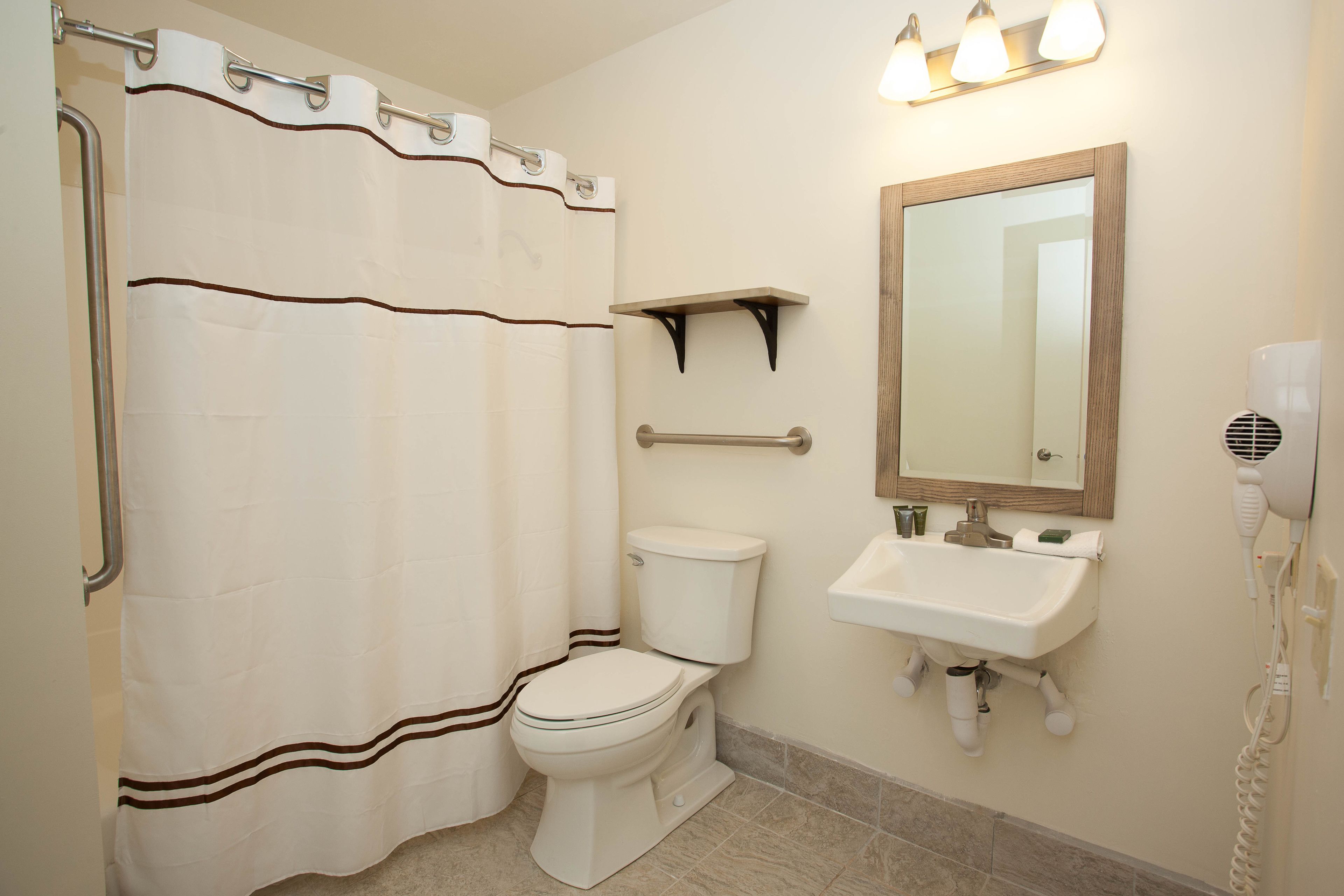 A bathroom with a white toilet, a shower curtain, a sink, a mirror, and a hairdryer.