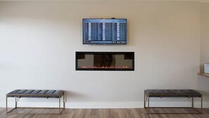A room with a flat-screen TV mounted above a fireplace, two benches in front, and a wooden floor. - Hotel Focus SFO (South San Francisco)