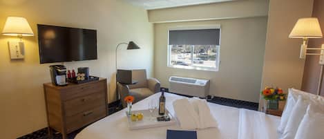 A hotel room with a bed, a desk, a chair, a TV, a window, and a lamp.