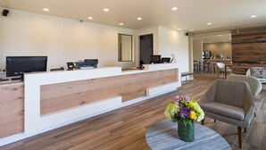 A reception area with a wooden reception desk, a television, and a flower vase. - Hotel Focus SFO (South San Francisco)