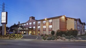 A multi-story hotel with a central entrance, a parking lot, and a signboard. - Hotel Focus SFO (South San Francisco)