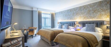 A hotel room with two beds, a desk with a lamp, a TV, and a window with curtains.