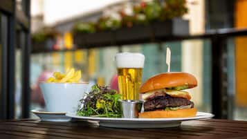 Uma refeição com hambúrguer, batatas fritas, salada e uma cerveja sobre uma mesa de madeira.