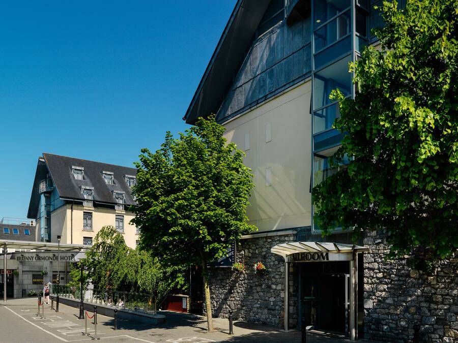 Un hotel con fachada de piedra, un edificio moderno de vidrio y una calle bordeada de árboles.