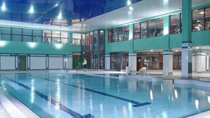 Une piscine intérieure avec des couloirs bien délimités, entourée d’un bâtiment moderne doté de grandes fenêtres et d’un sol carrelé.