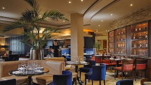 Un restaurant avec des tables rondes, des chaises bleues et un bar avec des étagères remplies de bouteilles.