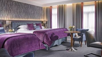 Hotelkamer met twee bedden, een zithoek met een ronde tafel en uitzicht op de stad door grote ramen.
