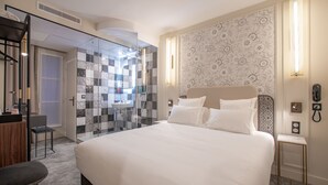 Habitación de hotel con una cama grande, un escritorio con una silla, un tocador con espejo y zona de ducha.