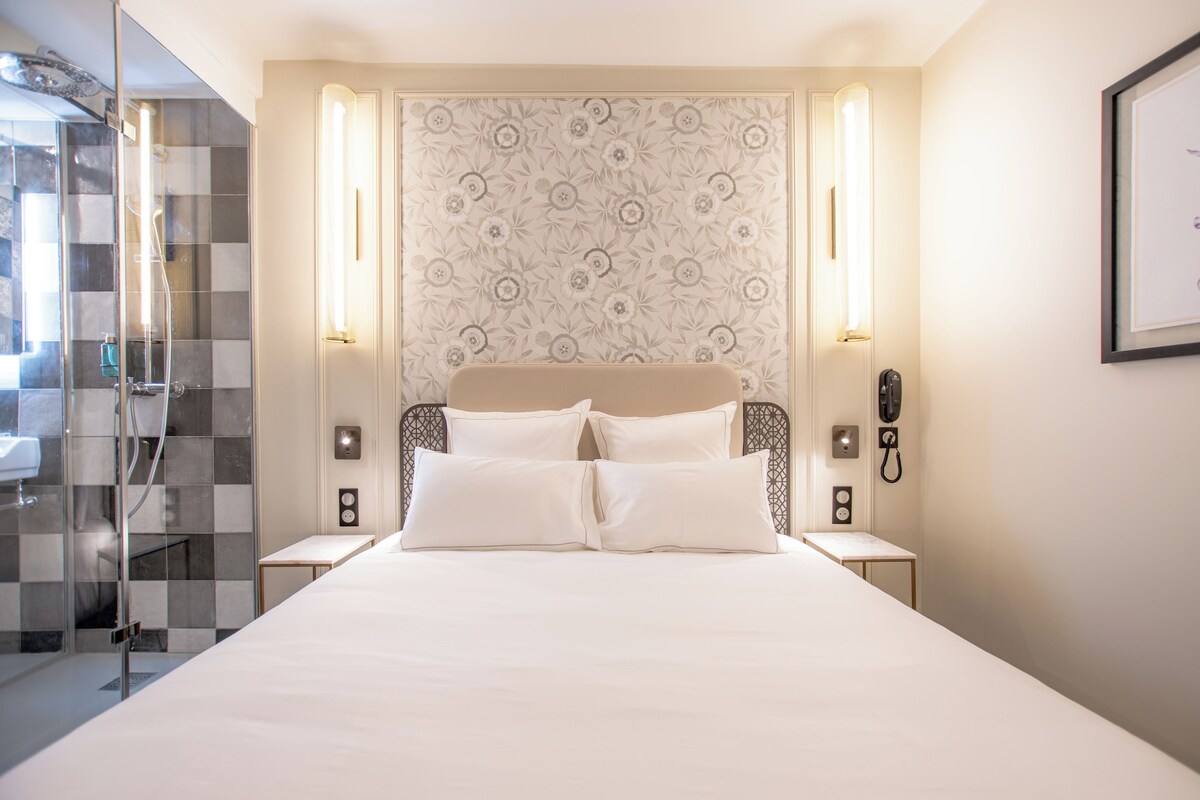 A hotel room with a large bed, a glass shower enclosure, and a patterned wall.