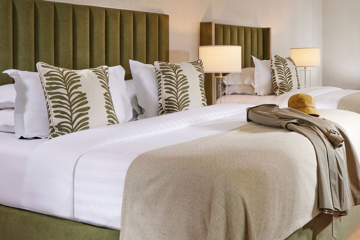 A hotel room with two beds, green headboards, white bedding, and two bedside lamps.